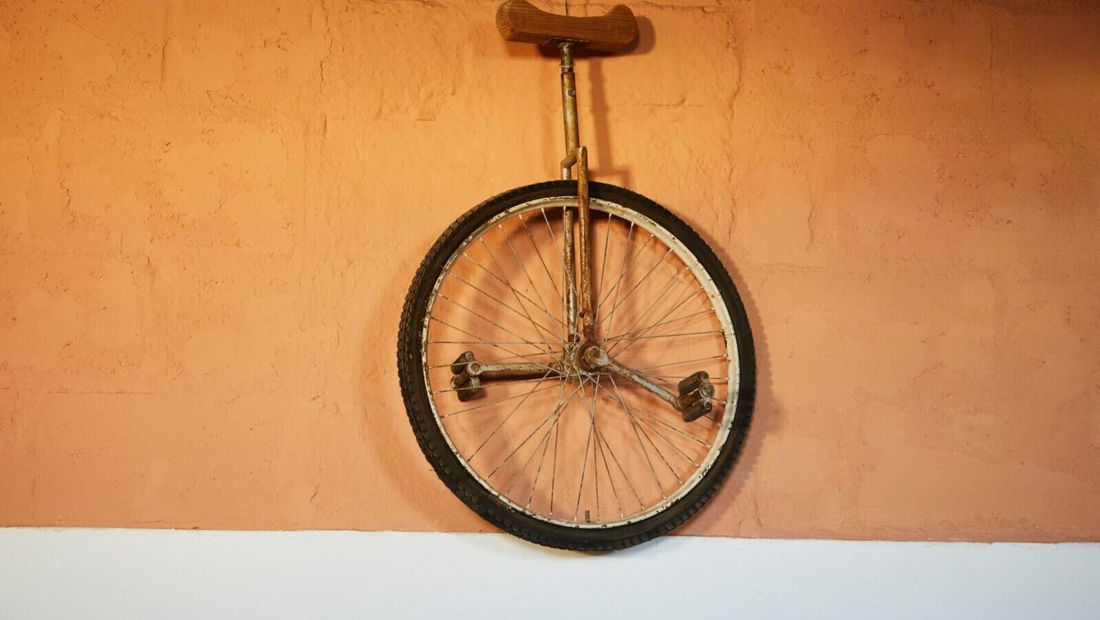Retro one wheel bicycle with rusty rack and brown seat hanging on brick orange wall
