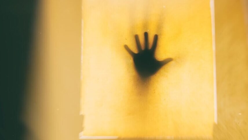 Artistic capture of a shadowy hand on a yellow backdrop, evoking suspense.